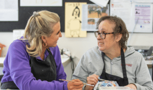 Kurrajong staff member and client smiling while painting a newspaper sculpture